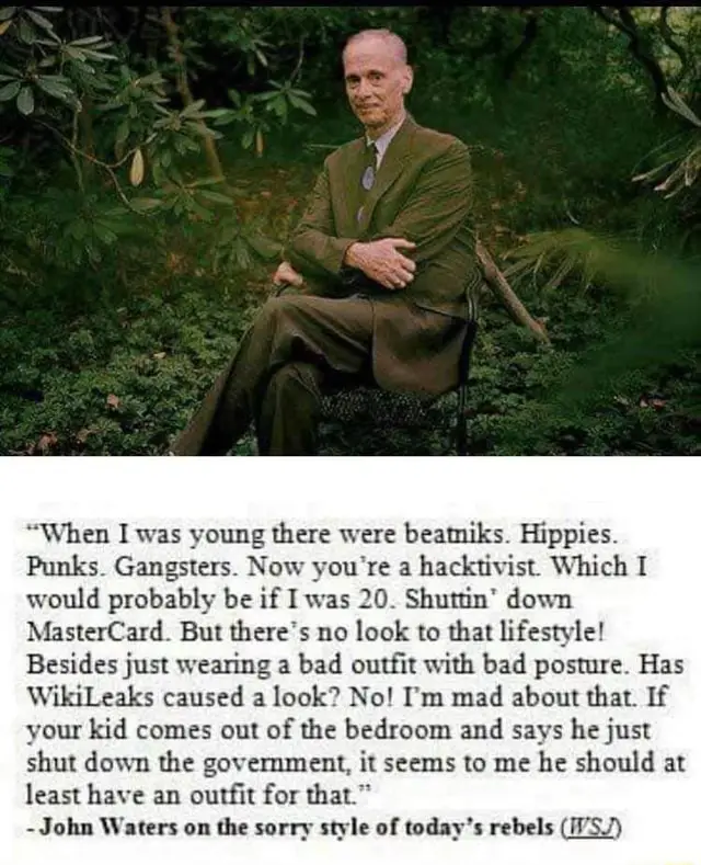 A man in a green suit sits in a chair surrounded by foliage. Overlaid text is a quote attributed to John Waters, mocking…
