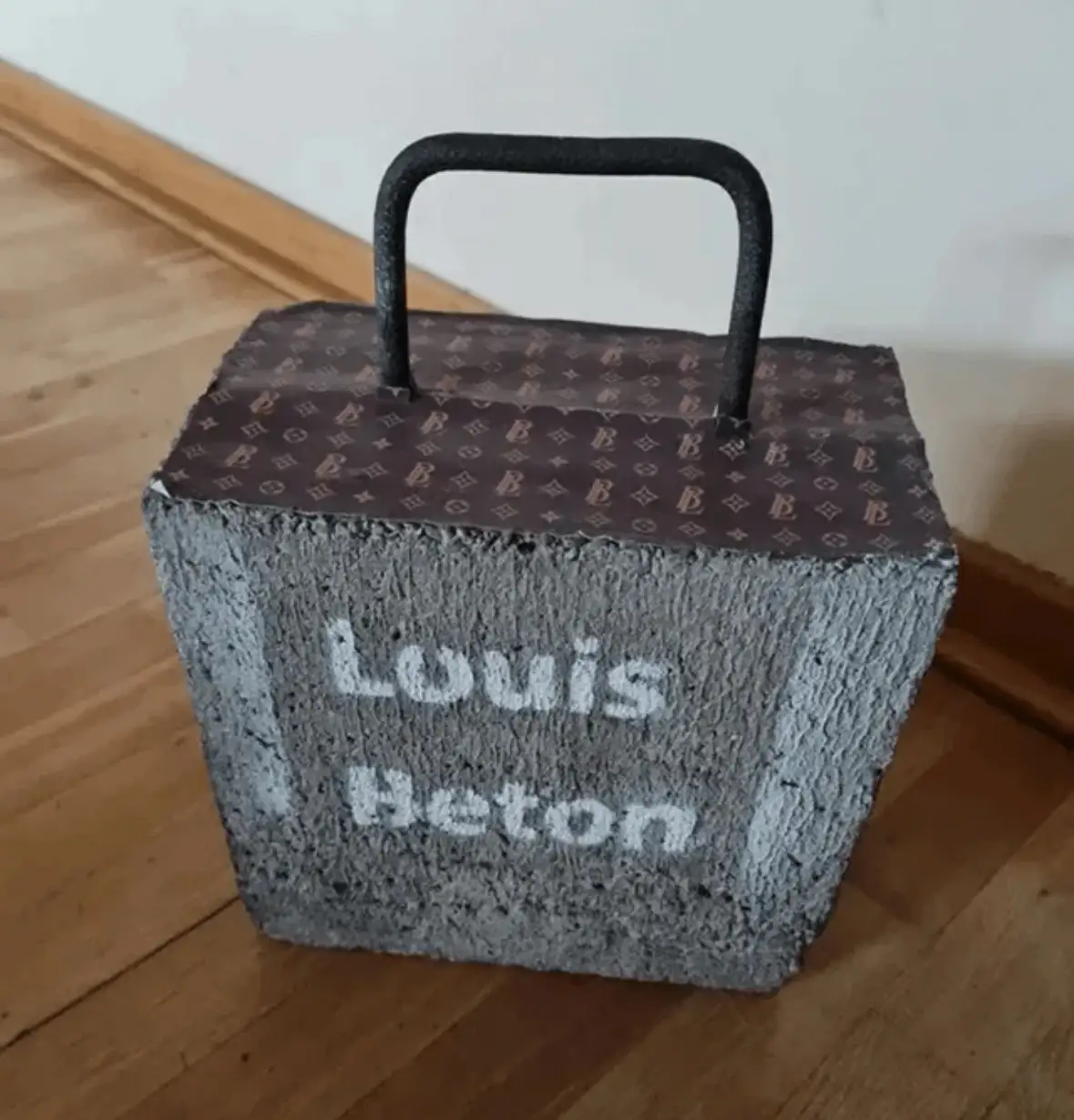 A gray concrete block sits on a wooden floor, wrapped with a brown Louis Vuitton monogram-patterned fabric and fitted with a…