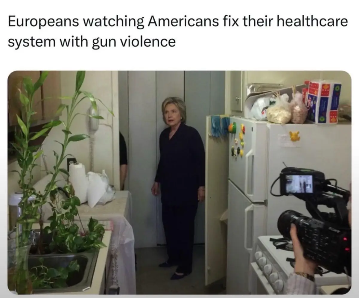 A woman in a dark outfit stands in a kitchen doorway, looking surprised as a camera operator films her from the right. The…