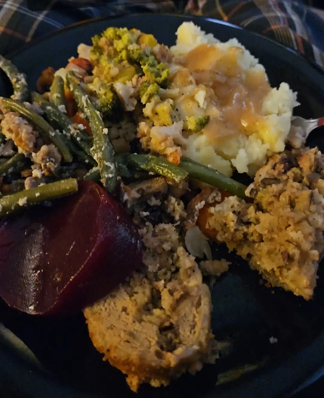 A close-up photo of a plate piled high with traditional Thanksgiving food including mashed potatoes with gravy, stuffing…