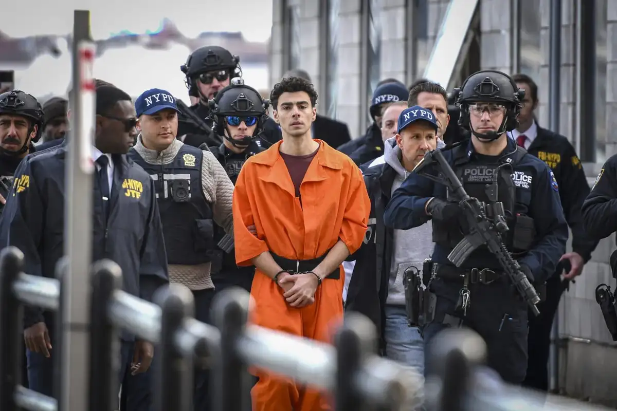 A young man in an orange prison jumpsuit stands with handcuffs, surrounded by heavily armed NYPD and FBI agents in tactical…