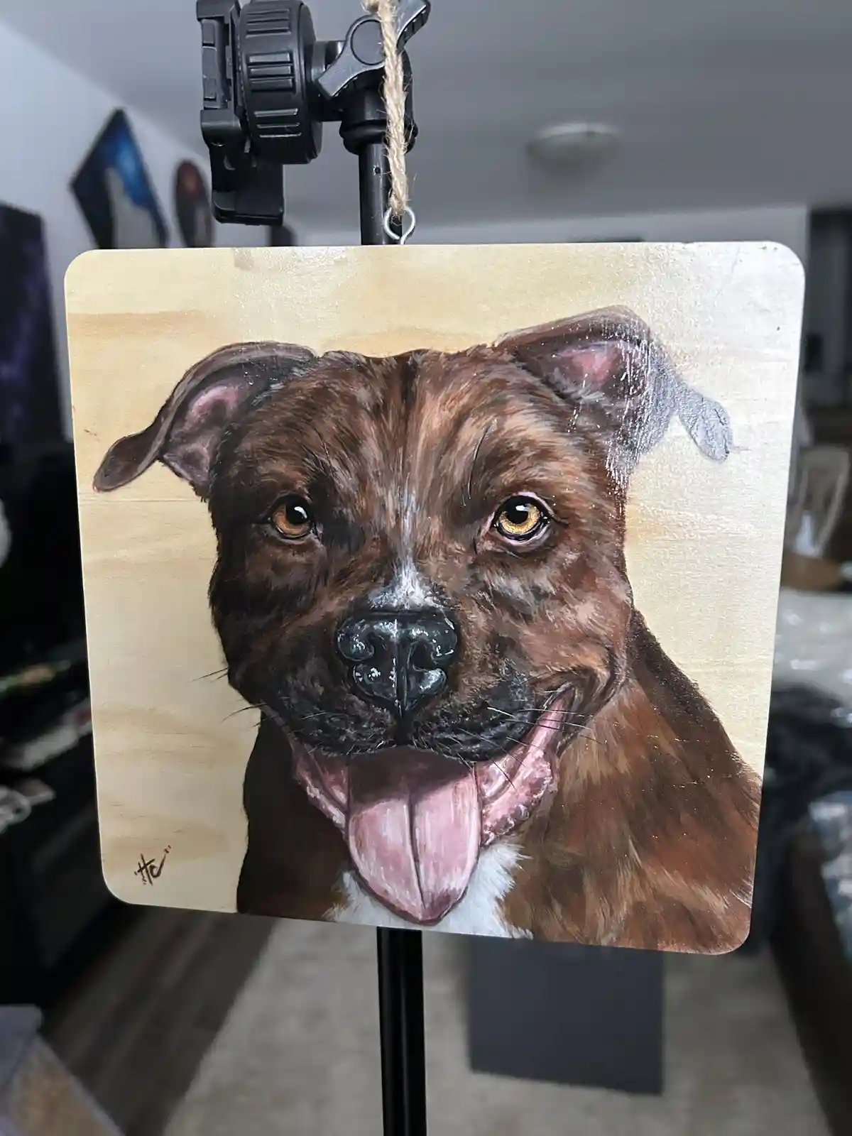 A painted portrait of a brown dog with floppy ears and a pink tongue hanging out, displayed on a wooden board hanging from a…