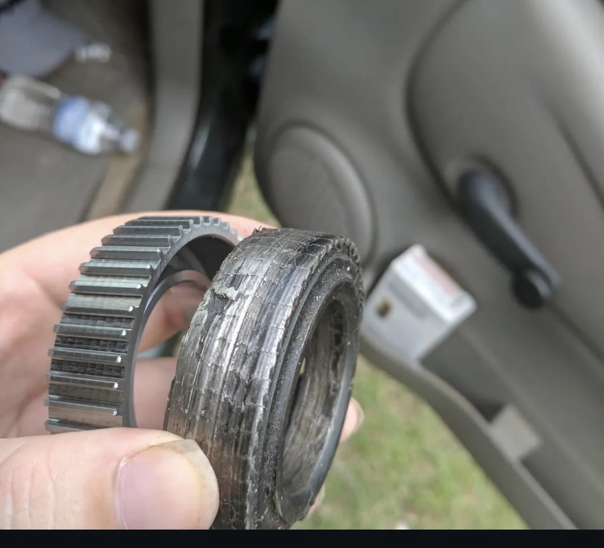 A hand holds two circular mechanical parts side-by-side: a clean metal gear with teeth and a heavily worn, cracked rubber…