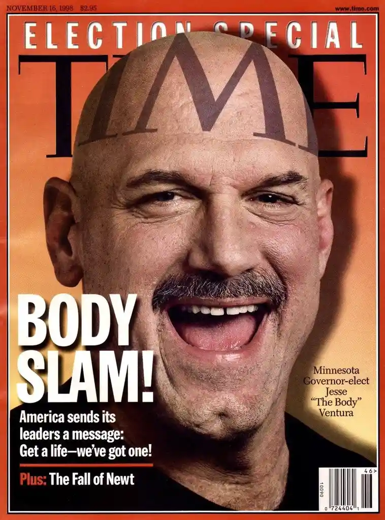 The image is the November 16, 1998, cover of Time magazine, featuring a bald man with a mustache and a wide grin. The…