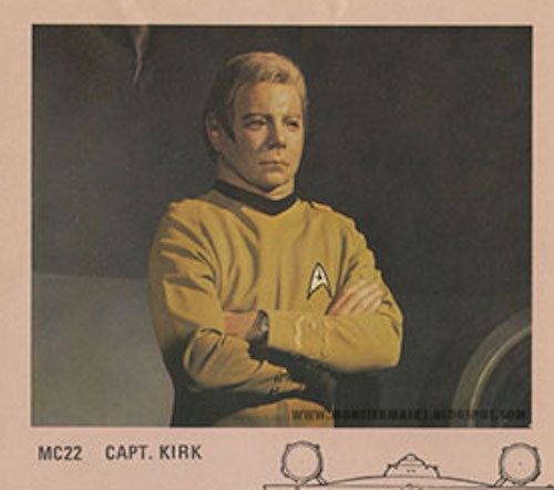 A vintage trading card-style image of Captain Kirk from Star Trek, shown with arms crossed in his yellow command uniform…