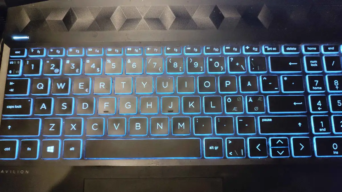 A close-up photo of a laptop keyboard with blue backlighting, showing all keys including function keys, number row, letter…