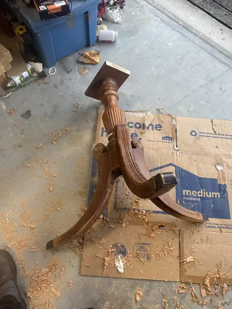 A close-up photo shows a wooden table leg with ornate, curved legs and a turned top, resting on a cardboard box covered in…