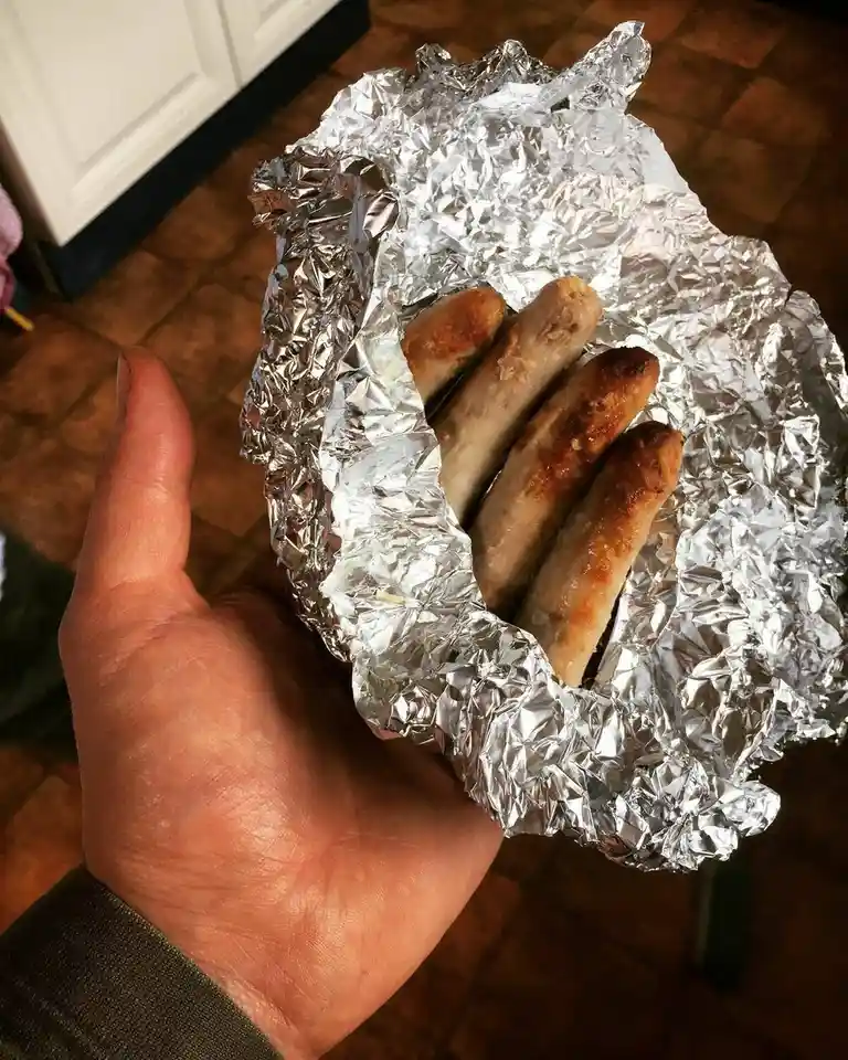 A person's hand holds a crumpled foil packet containing four cooked sausages, with the text 'i made my own sausage'…