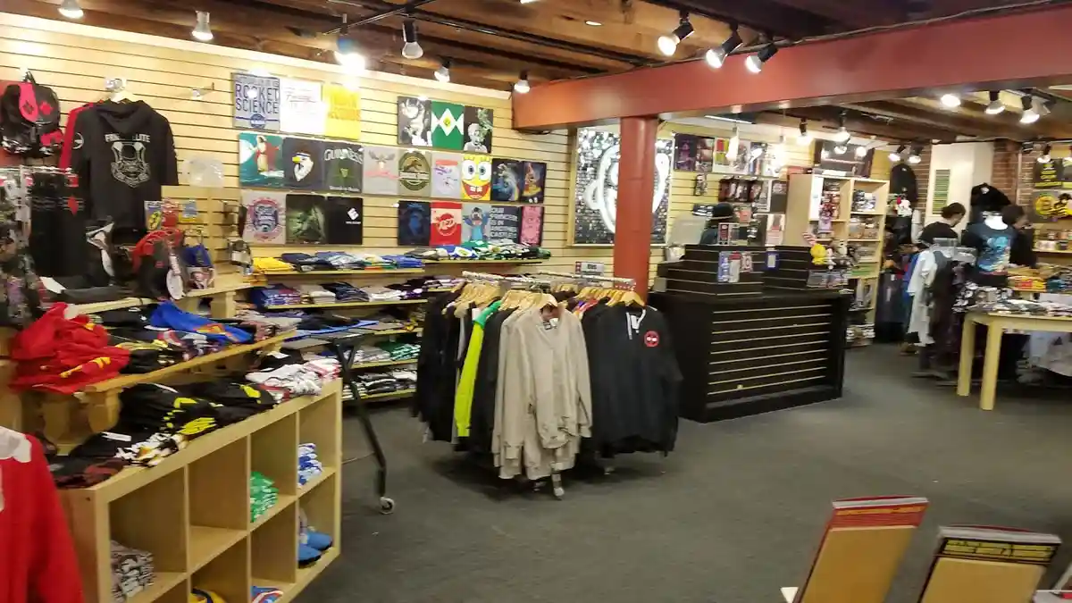 An interior shot of a retail store filled with merchandise, including t-shirts, hoodies, and posters on wooden walls. The…