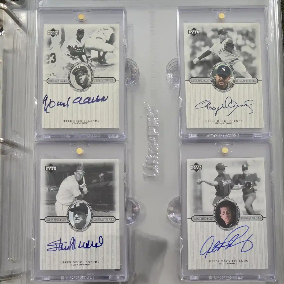 Four Upper Deck Legends baseball trading cards, each signed by a different player, are displayed in a binder. The cards…