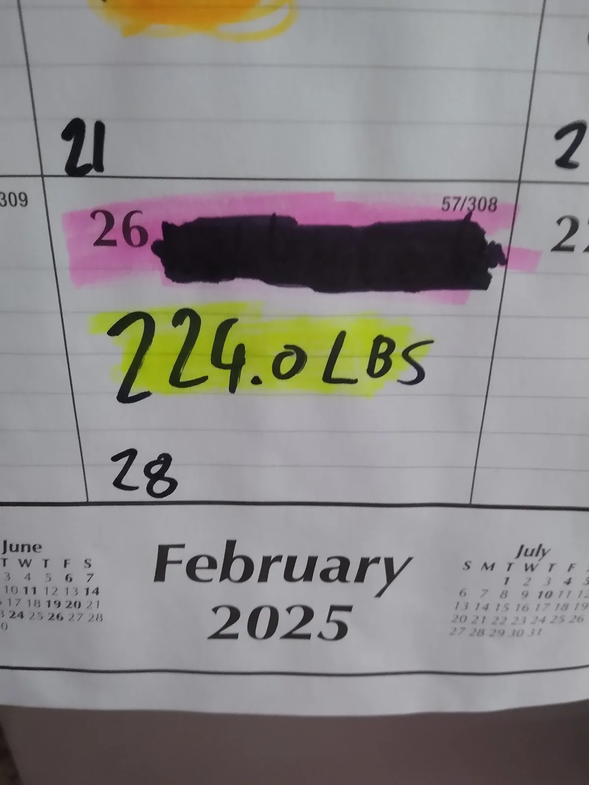 A close-up of a printed calendar for February 2025, showing the date 26th is highlighted in pink and has a black marker…