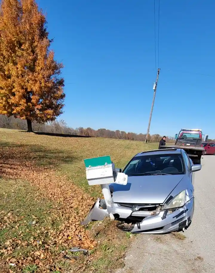 A silver sedan is severely damaged after crashing into a green and white mailbox, which is now detached and leaning against…