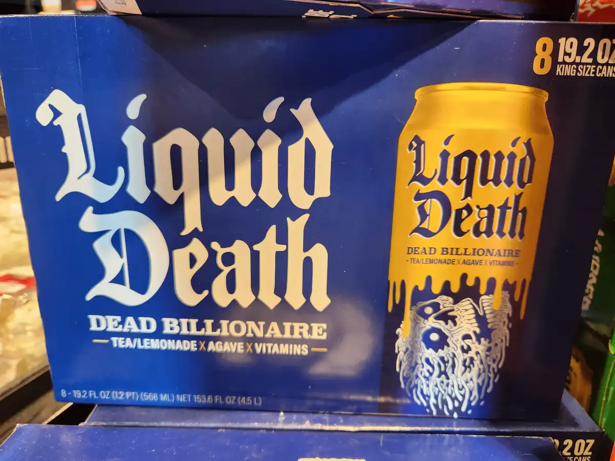 A close-up of a blue box of 'Liquid Death' brand beverage, specifically the 'Dead Billionaire' flavor, which is described as…
