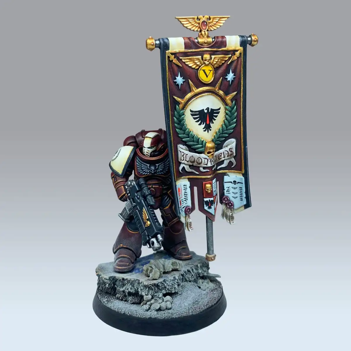A painted miniature of a Space Marine from Warhammer 40,000, specifically a Blood Ravens Chapter, stands on a rocky base…