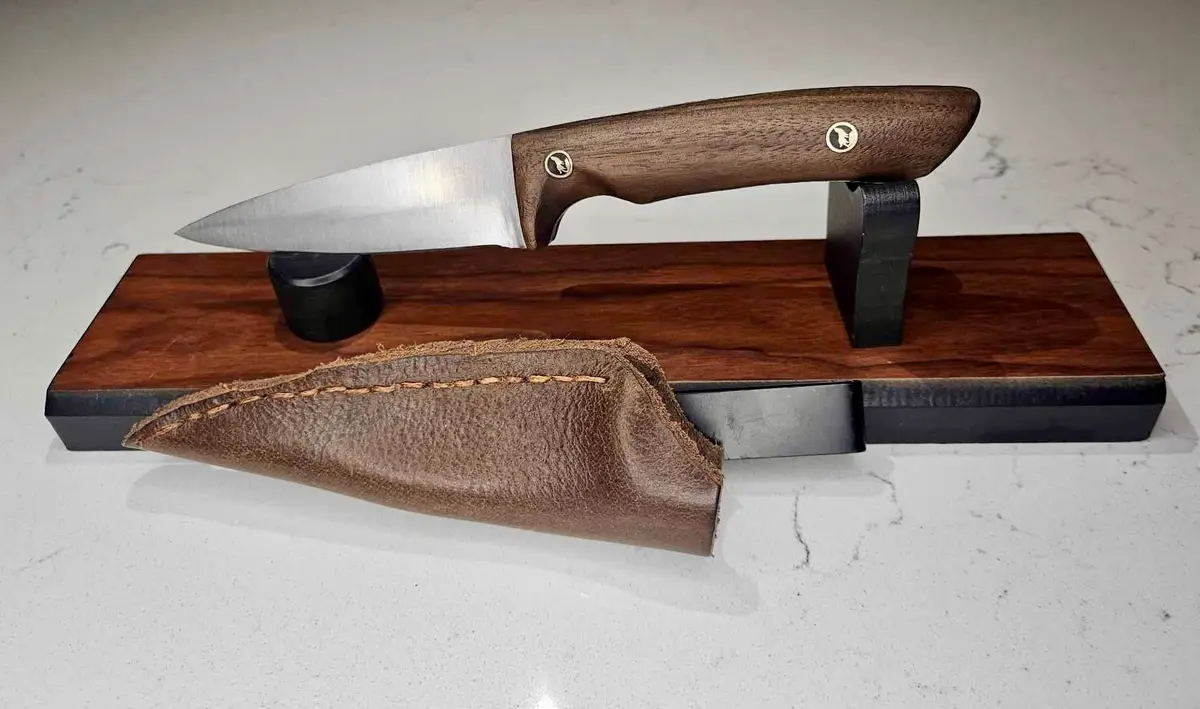 A high-quality knife with a wooden handle and metal blade rests on a dark wooden display stand with black supports, next to…
