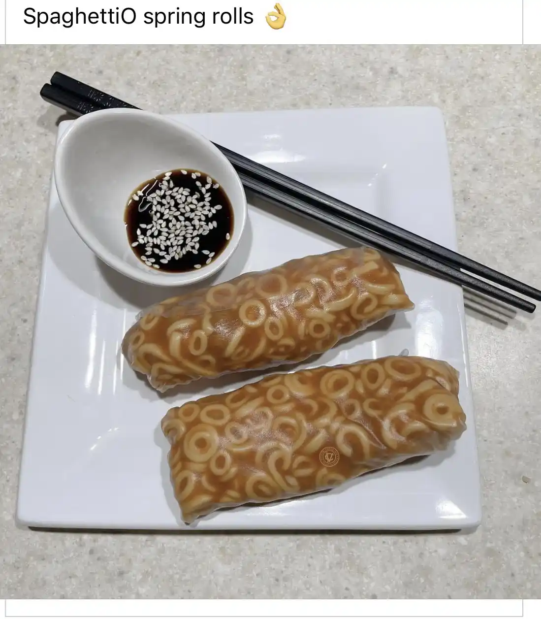 Two spring rolls with a visible SpaghettiOs pattern on their translucent wrapper sit on a white plate next to a small bowl…
