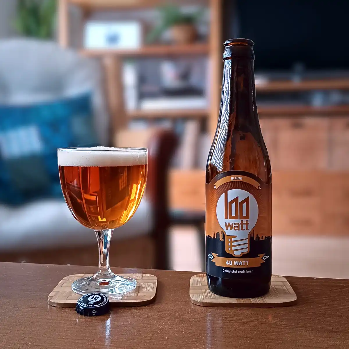 A brown beer bottle labeled '40 WATT' and 'Delightful craft beer' sits next to a glass of amber beer with a white head, both…