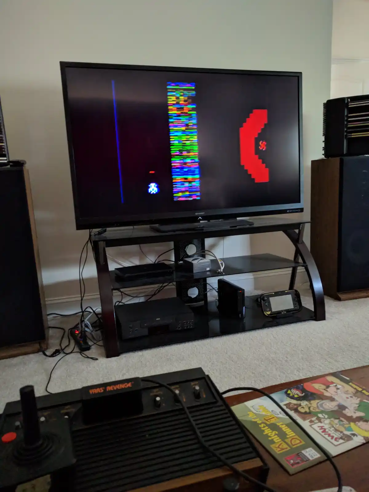 A modern TV displays a heavily glitched, colorful vertical artifact next to a red pixelated ghost from Pac-Man, while a…