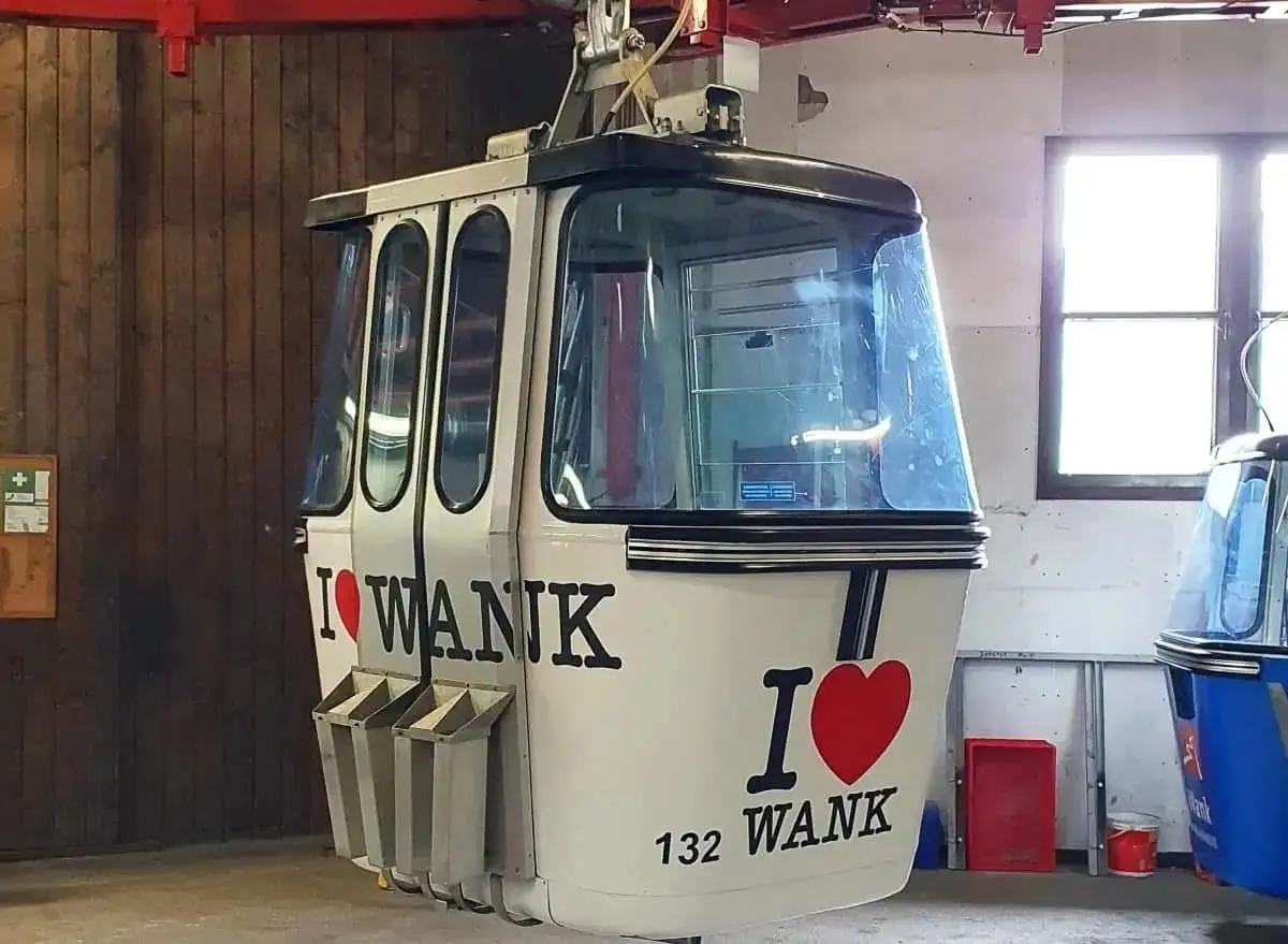 A white cable car cabin, parked indoors, has the phrase 'I ❤️ WANK' painted in large black letters with a red heart on both…