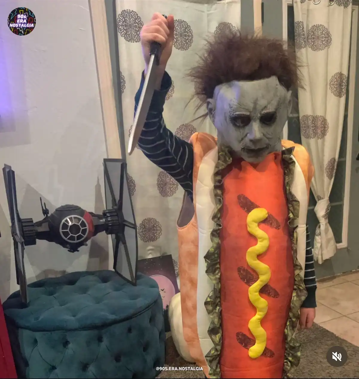 A child dressed as Michael Myers from Halloween, wearing a hot dog costume with mustard, holds a knife aloft. To the left, a…