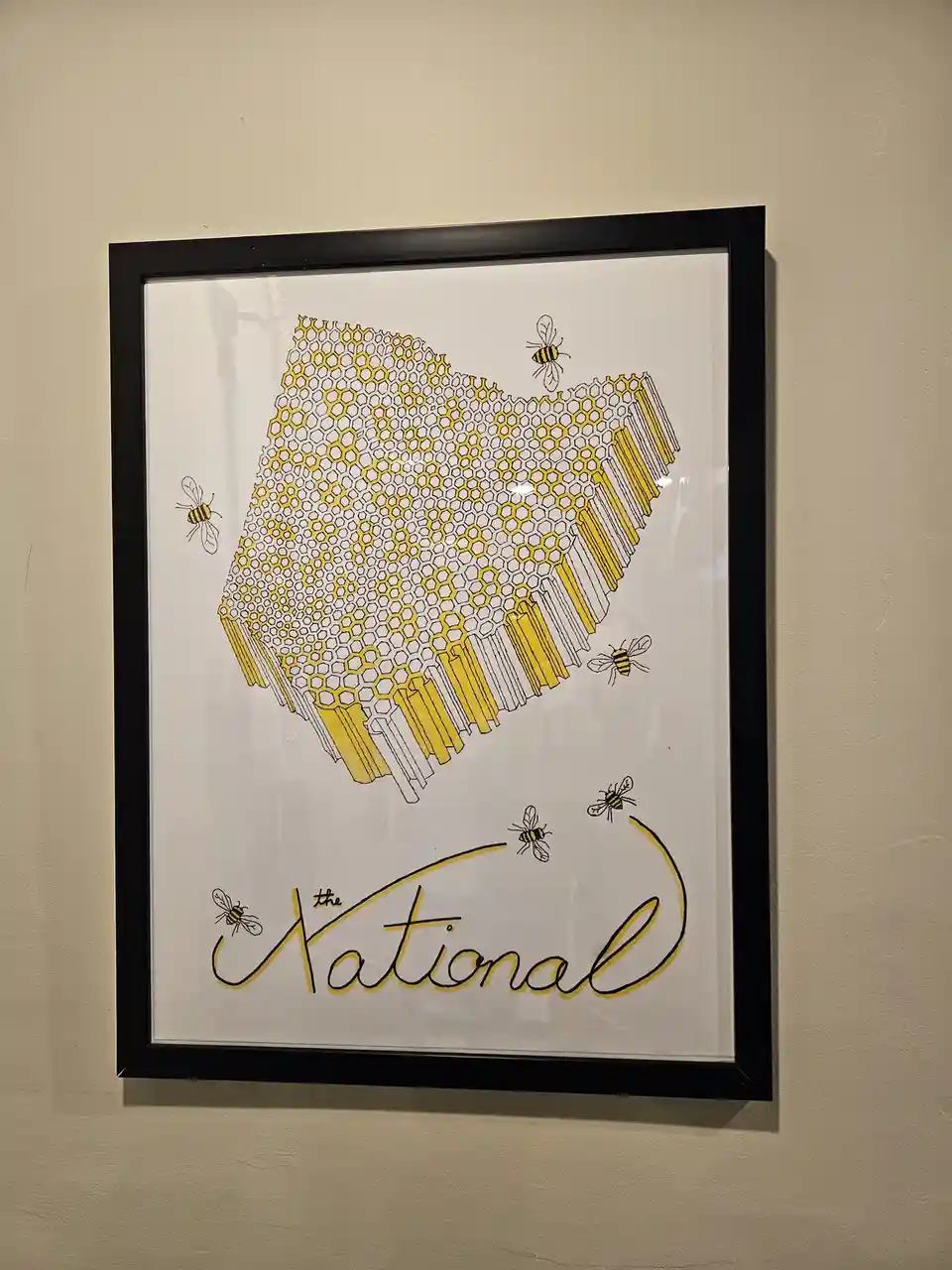 A framed art print on a beige wall shows a stylized 3D honeycomb structure with yellow and white hexagons, surrounded by…