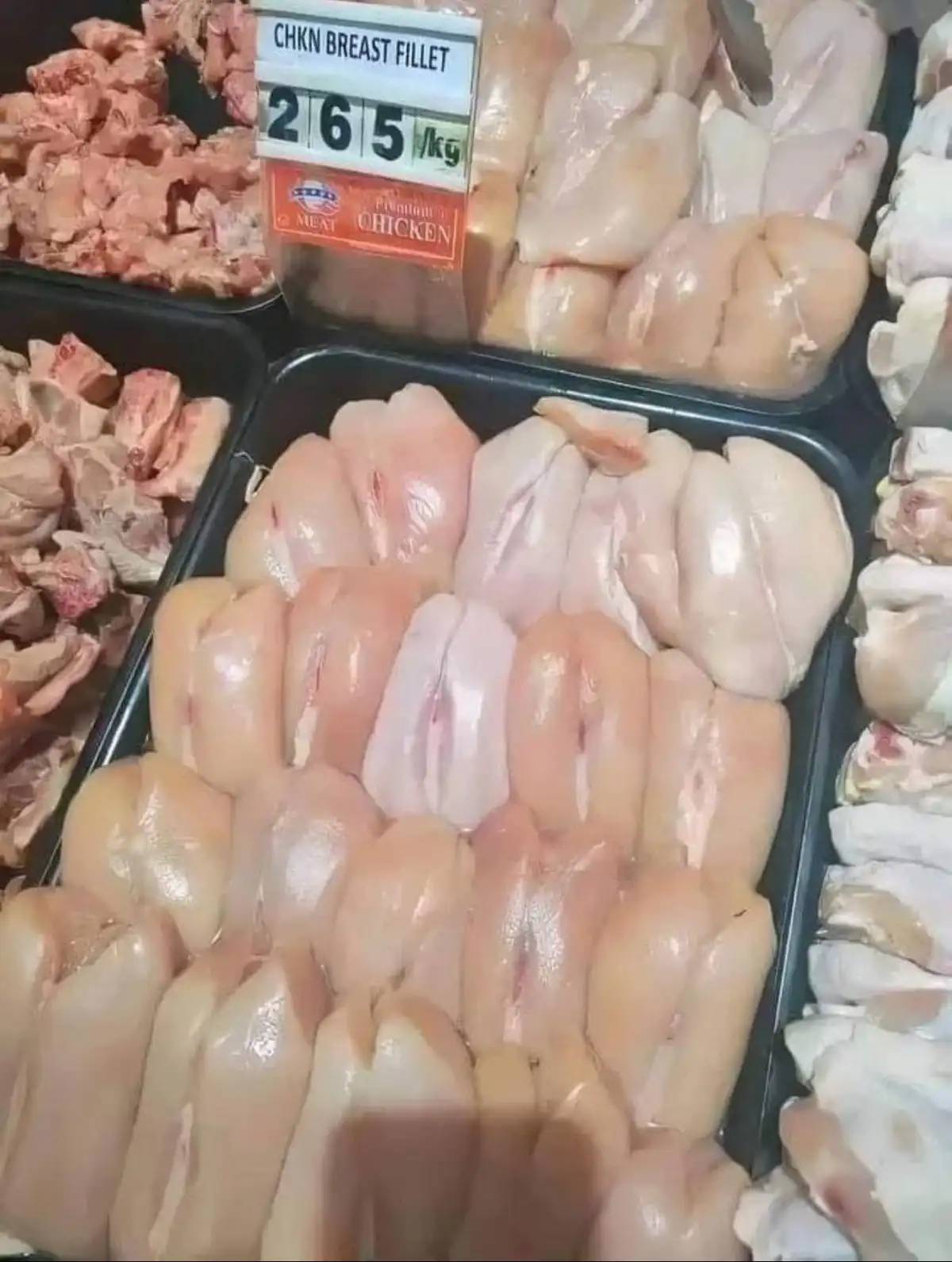 A supermarket meat display shows raw chicken breast fillets arranged in black trays, with a price tag reading 'CHKN BREAST…