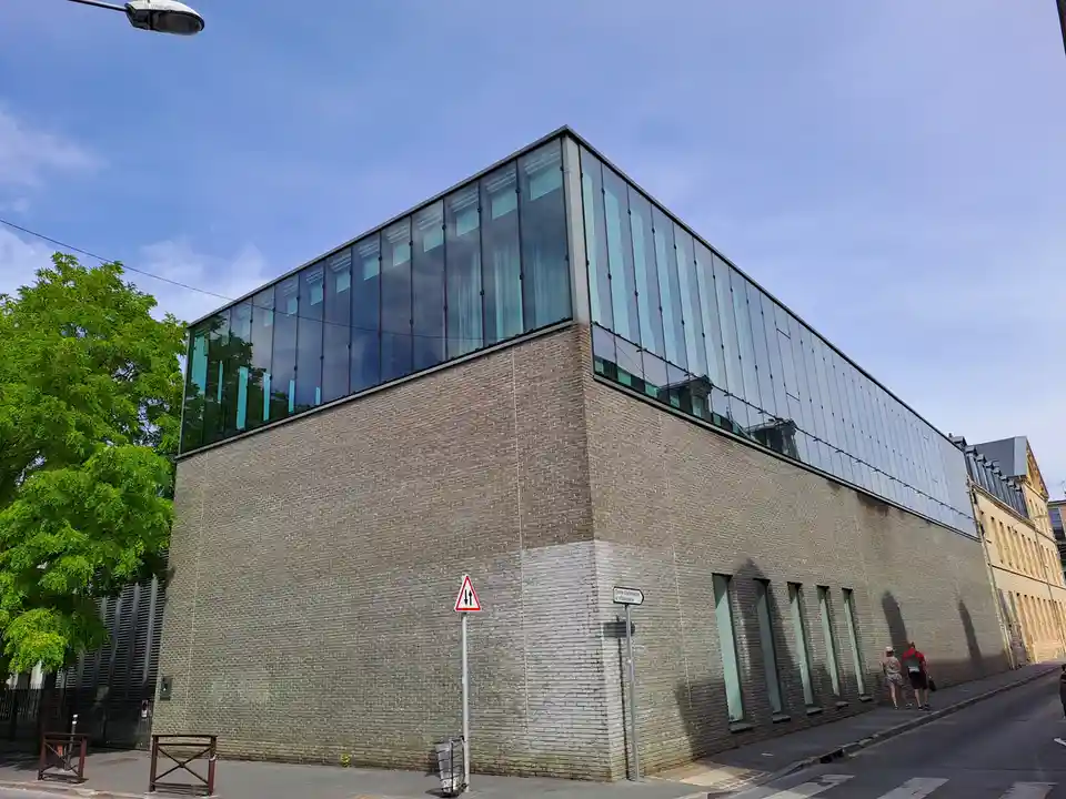 A modern building with a brick base and glass upper level, featuring a street sign that reads 'Centre d'Information et…