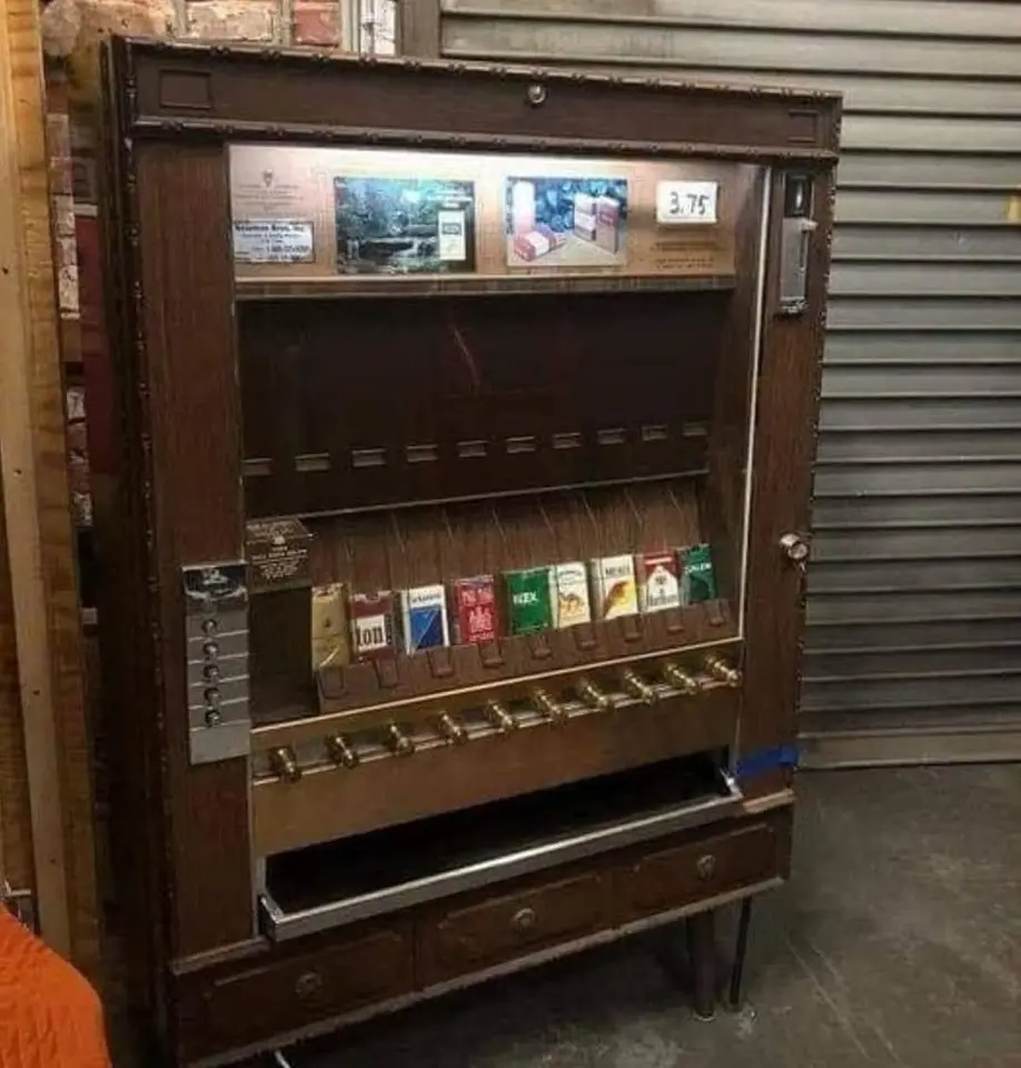 An old-fashioned wooden cigarette vending machine with a price tag of 3.75, displaying various cigarette brands in its…