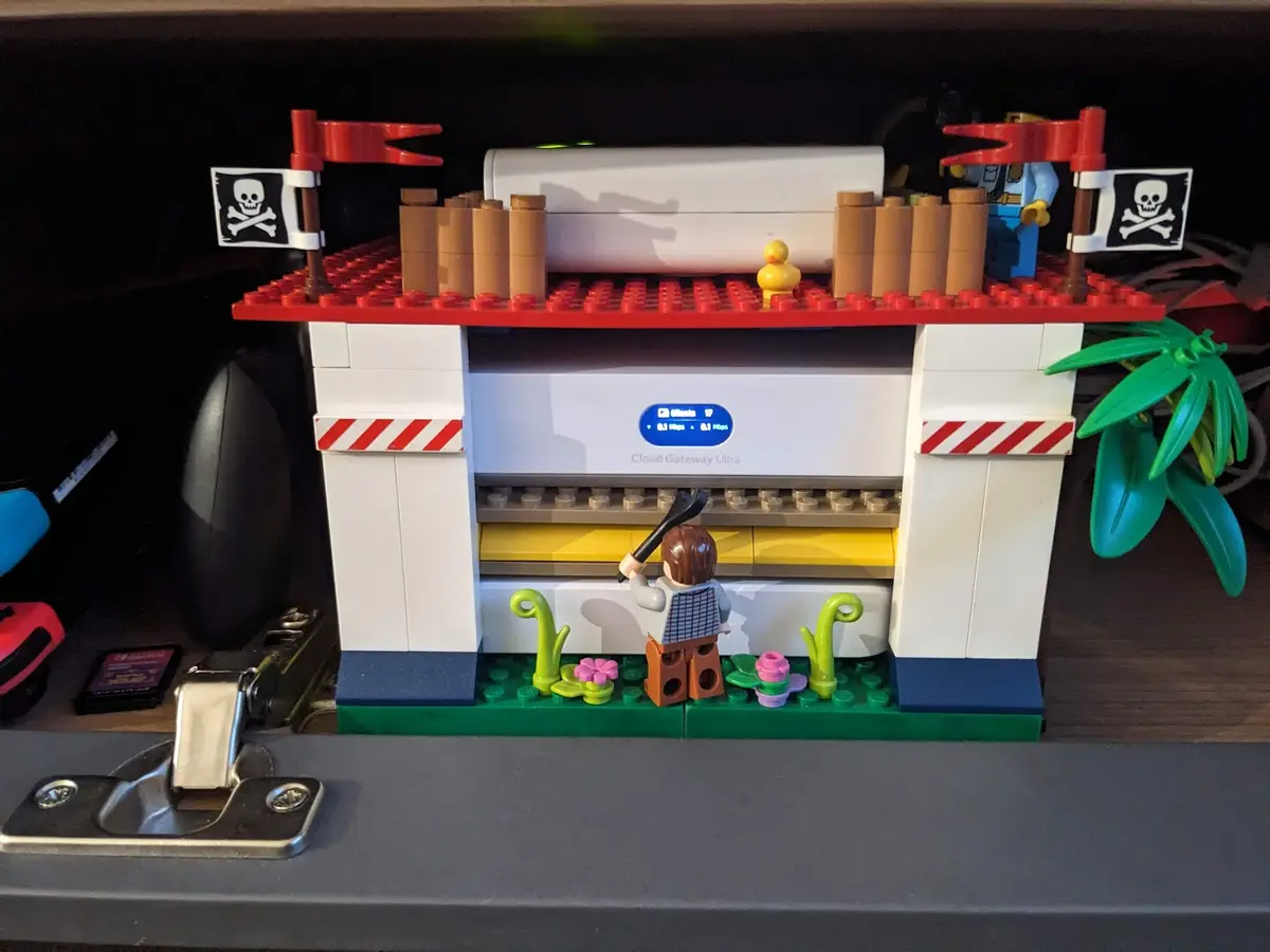 A Lego diorama depicts a pirate-themed setup around a real-world 'Cloud Gateway Ultra' network device, with pirate flags, a…