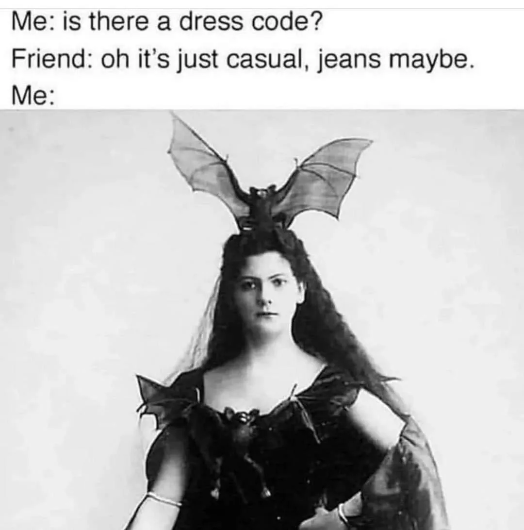 A black-and-white vintage photograph shows a woman with long dark hair wearing a dark dress adorned with bat-wing-like…