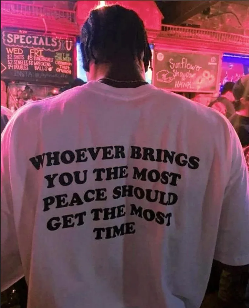 A person viewed from behind wears a white t-shirt with bold black text reading 'WHOEVER BRINGS YOU THE MOST PEACE SHOULD GET…