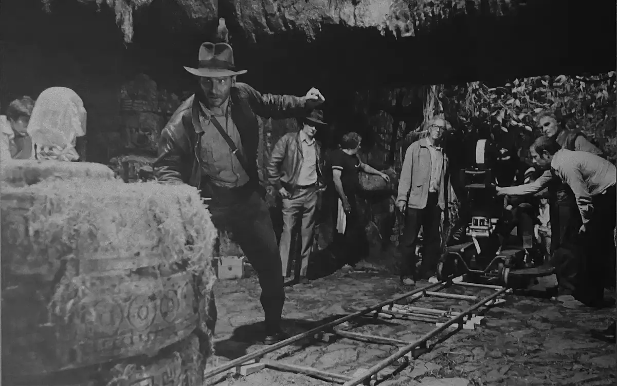 A black-and-white behind-the-scenes photo from the filming of 'Raiders of the Lost Ark' shows actor Harrison Ford as Indiana…