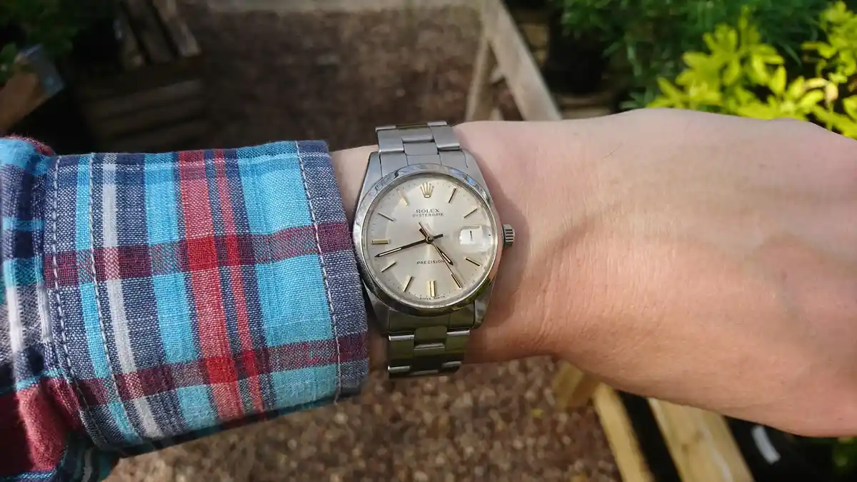 A close-up photo shows a person's wrist wearing a silver Rolex Oysterdate Precision watch with a light-colored dial and…