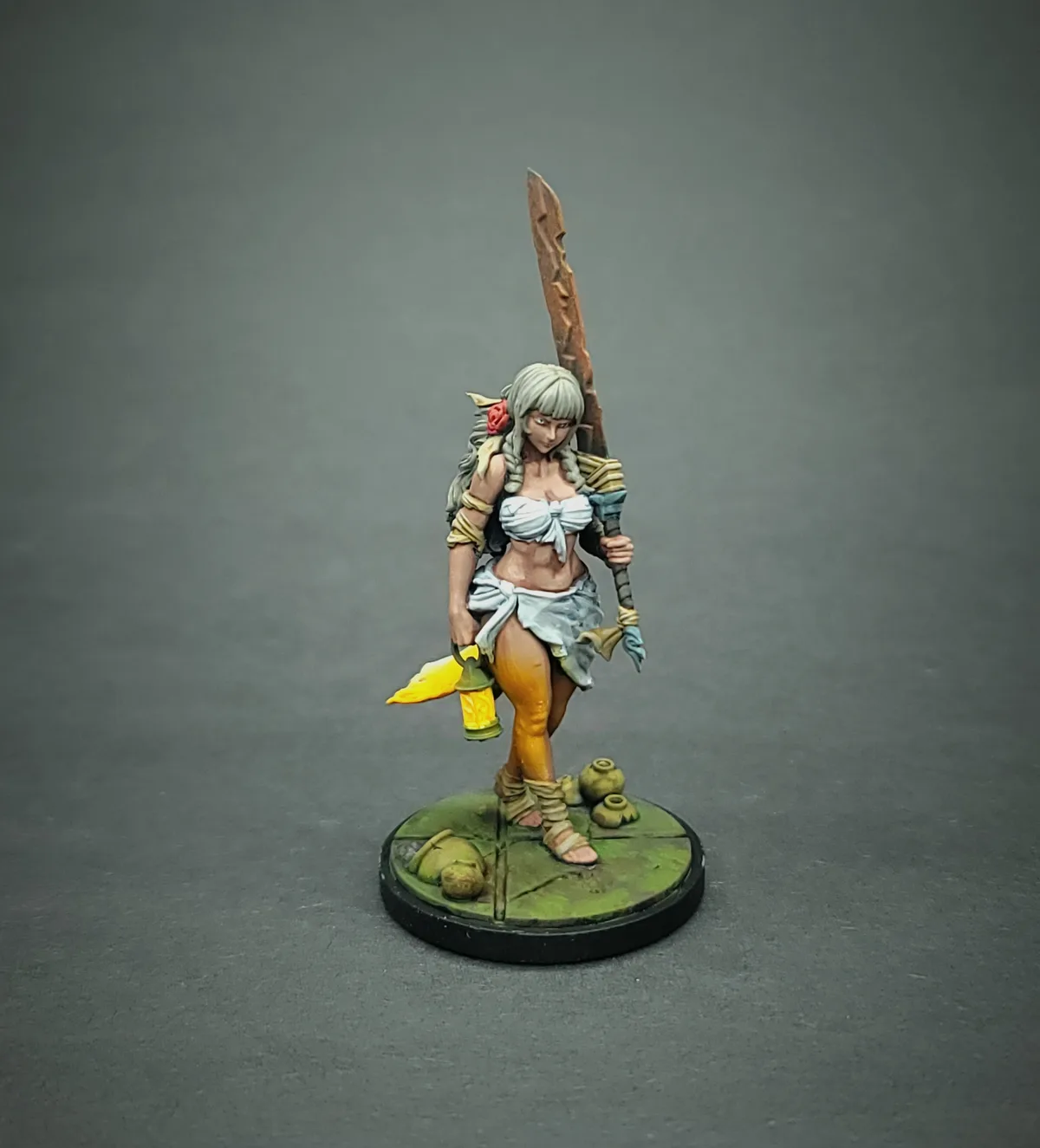A painted fantasy miniature of a female warrior with silver hair, holding a large sword over her shoulder and a lit lantern…