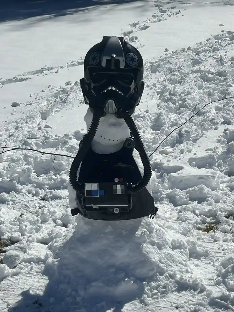 A snowman is constructed with a black stormtrooper helmet from Star Wars, complete with Imperial insignia, and a black chest…