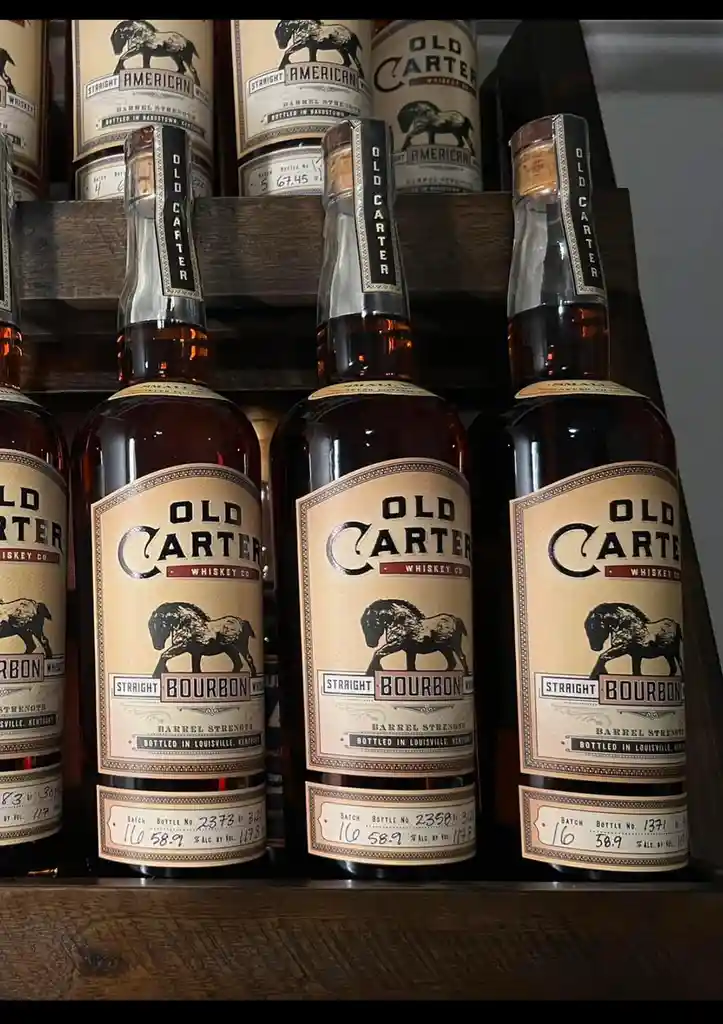 Several bottles of Old Carter Whiskey Co. bourbon are displayed on wooden shelves, each labeled with 'Straight Bourbon'…