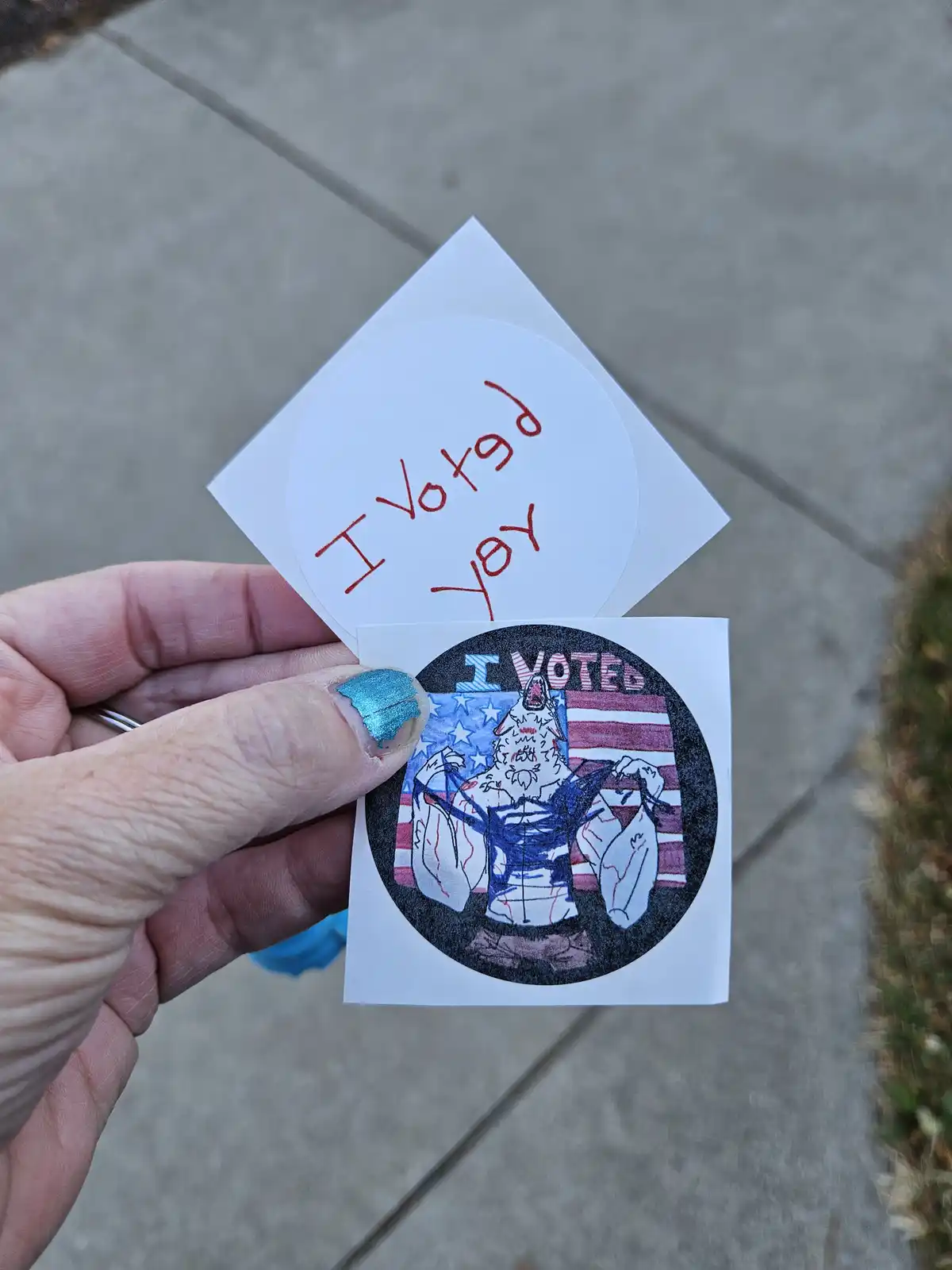 A hand holds two custom 'I Voted' stickers. The top one is a plain white circle with red handwritten text reading 'I Votgd…
