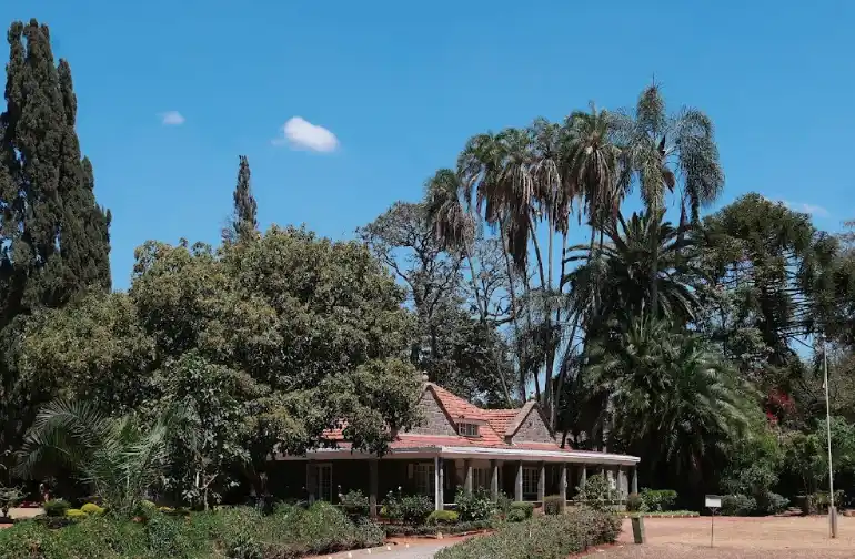 A serene photo of a stone house with a red-tiled roof nestled among lush green trees and palm trees under a clear blue sky…