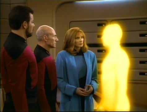 three star trek crew members stand in a ship corridor, looking toward a glowing yellow humanoid silhouette. the overlaid…