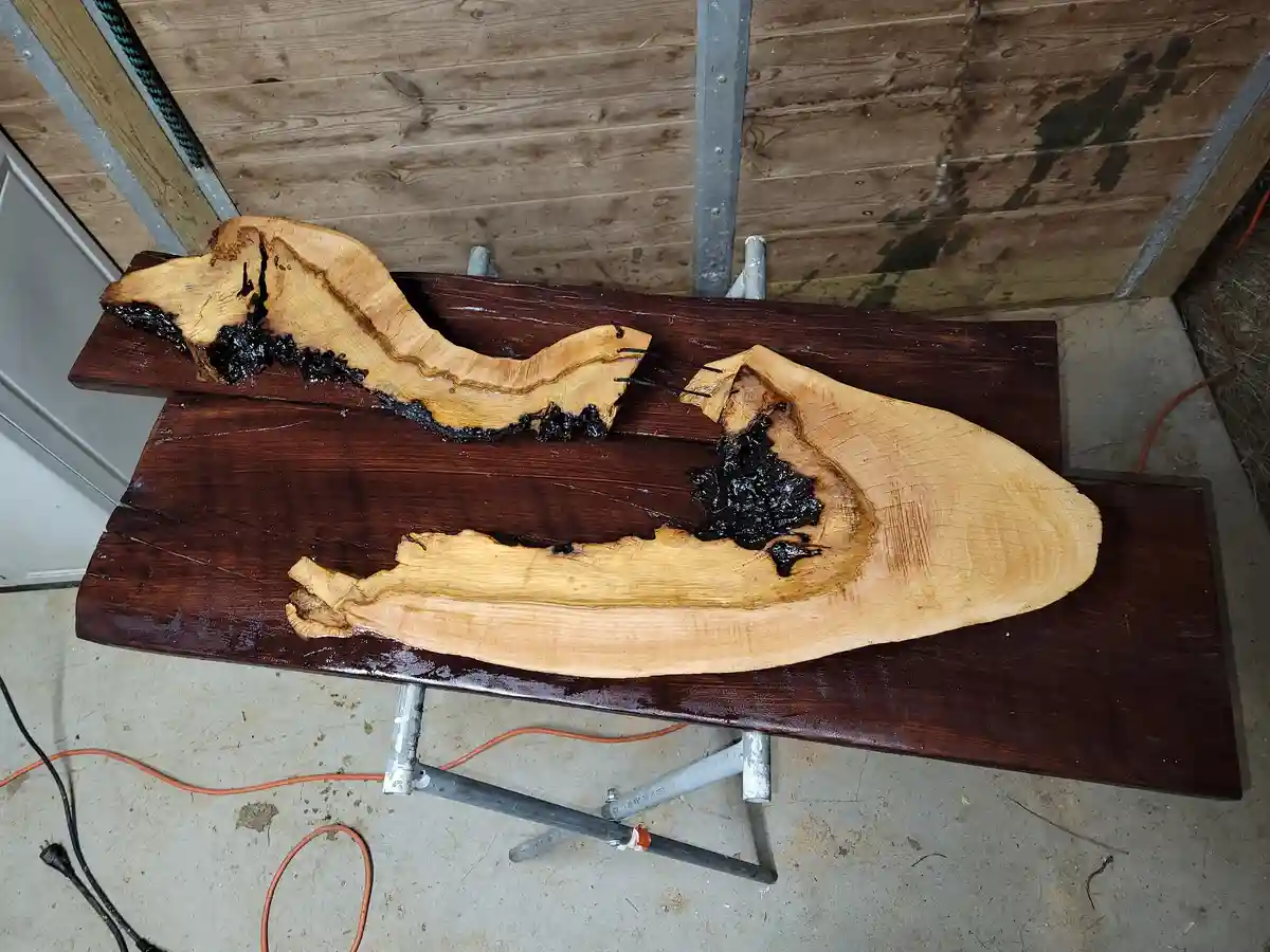 Two large, irregularly shaped wooden planks, resembling boat hulls, are laid on a dark wooden workbench. The wood has a…