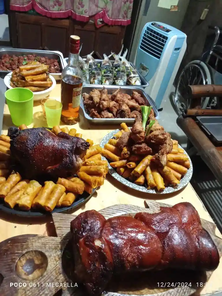 A table is covered with an abundant spread of food including roasted chicken, fried chicken, spring rolls, grilled fish, and…