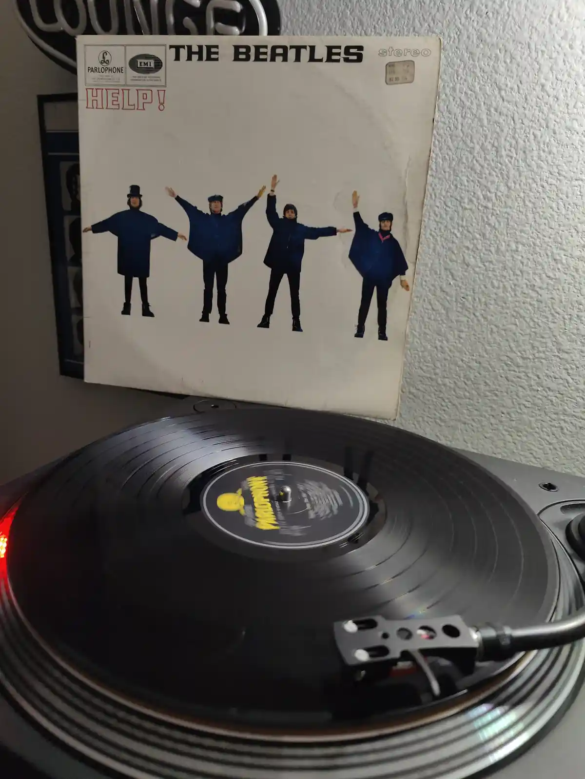 A vintage vinyl record of The Beatles' album 'Help!' is shown with its cover propped up above a turntable playing the…