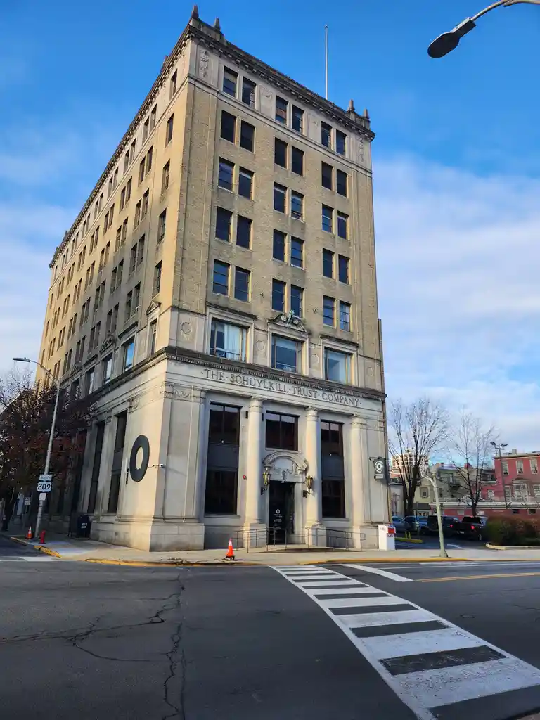 A tall, historic brick building with ornate stone detailing and columns at its corner entrance, bearing the engraved text…