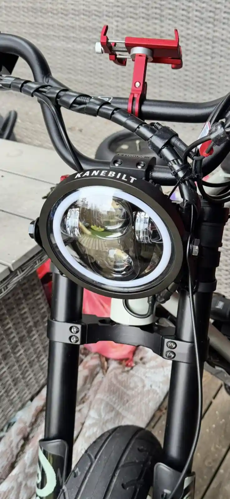 A close-up photo of a bicycle's front end, featuring a large, round, black 'KANEbilt' brand headlight with a bright white…