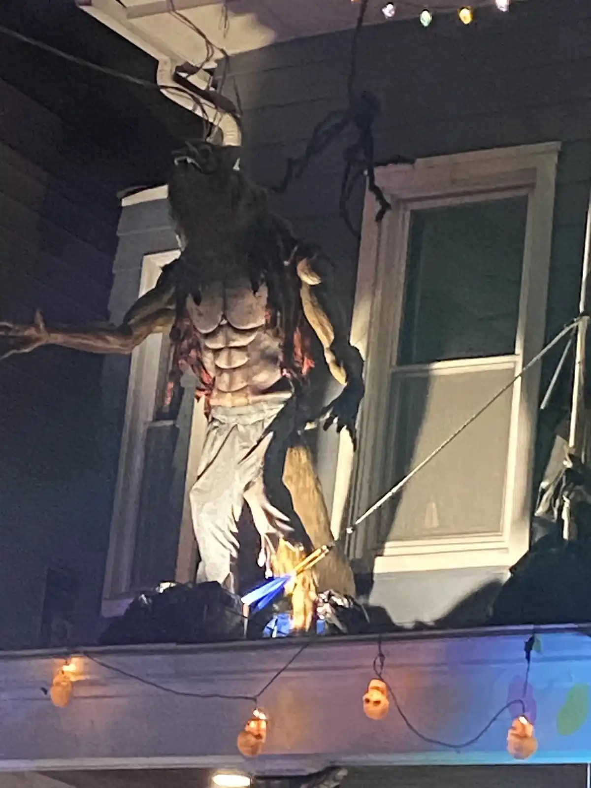A large, grotesque Halloween monster decoration with a muscular torso, animalistic head, and tattered clothing is mounted on…