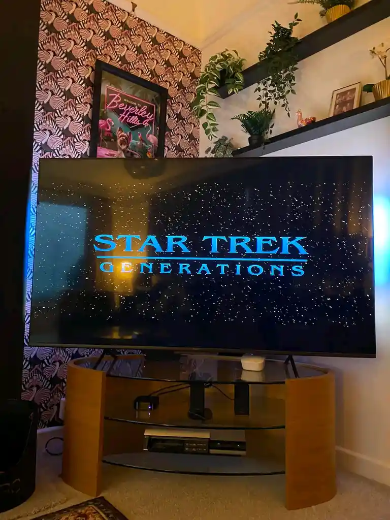 A large flat-screen TV in a cozy living room displays the title card for 'Star Trek Generations' against a starfield…