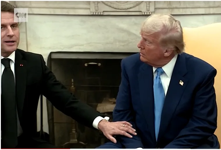a man in a black suit places his hand on the shoulder of another man in a blue suit seated in an ornate room with a…