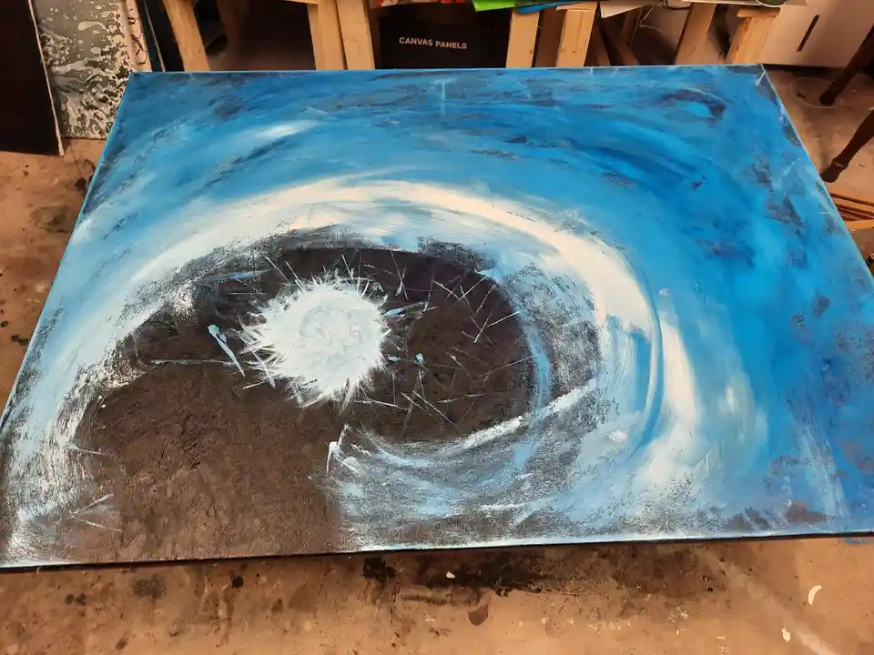 A large, unfinished painting on a canvas depicts a stylized human eye with a blue iris, white sclera, and dark pupil, lying…