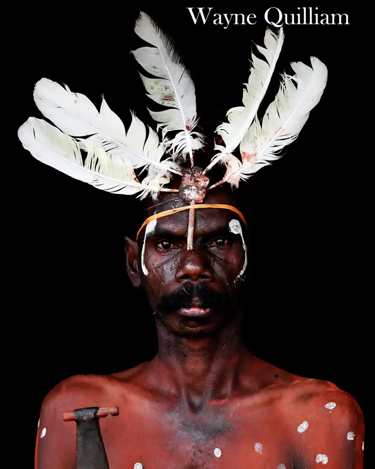 A portrait of a man with dark skin, adorned with traditional white body paint and red ochre, wearing a headdress of white…