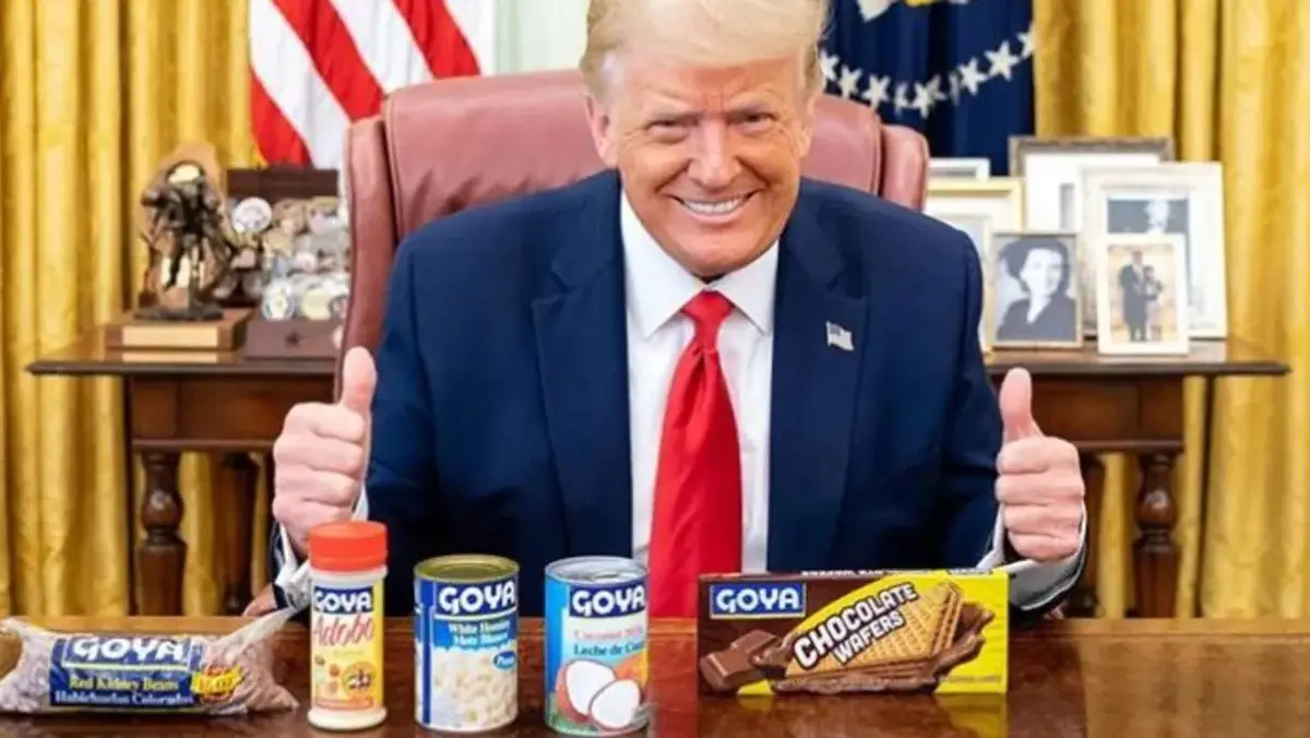 Donald Trump sits at a desk in the Oval Office, giving two thumbs up, with several Goya brand food products arranged in…